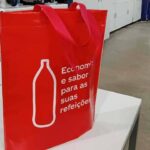 Sacola vermelha feita em TNT com alças largas e frase impressa, exemplo de sacolas personalizadas sustentáveis utilizadas por empresas.