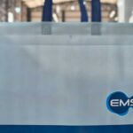 Sacola branca e azul de TNT com logo da empresa, exemplo de sacolas personalizadas grandes marcas usadas em ações corporativas sustentáveis.