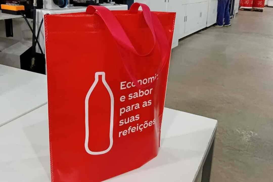 Sacola vermelha feita em TNT com alças largas e frase impressa, exemplo de sacolas personalizadas sustentáveis utilizadas por empresas.