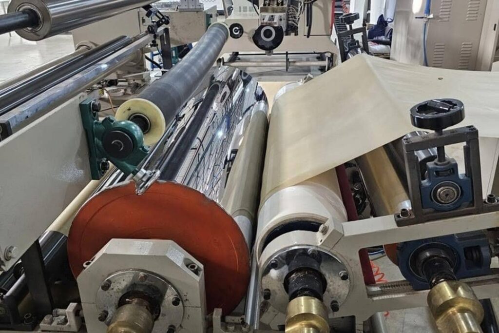 M&aacute;quina industrial em opera&ccedil;&atilde;o durante o processo de fabrica&ccedil;&atilde;o de sacolas sustent&aacute;veis para empresas, mostrando tecnologia e precis&atilde;o na produ&ccedil;&atilde;o.
