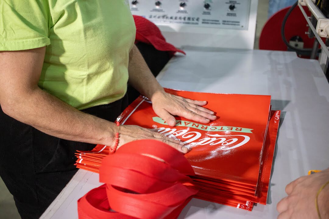Processo de produção de sacolas reutilizáveis personalizadas, mostrando o manuseio e acabamento de embalagens sustentáveis para o varejo.
