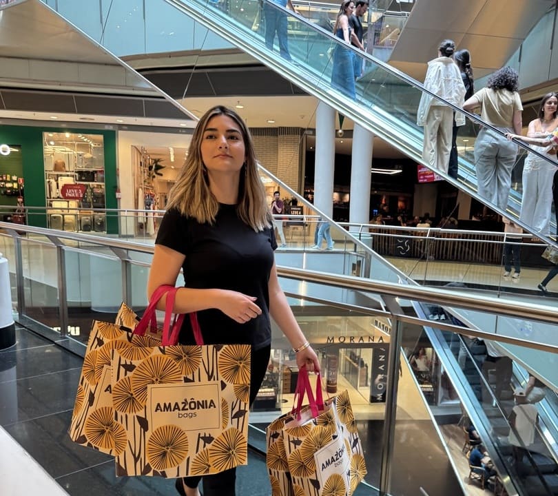 Mulher caminhando em um shopping segurando sacolas sustentáveis para empresas da Amazônia Bags, destacando o uso de embalagens reutilizáveis que fortalecem a presença da marca no varejo.