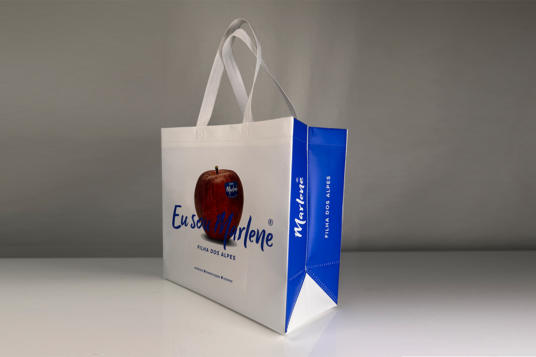Sacola sustentável personalizada da Amazônia Bags, em TNT branco com laterais azuis, alças resistentes e estampa de maçã, posicionada sobre fundo neutro.