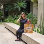 Mulher loira sentada em um banco segura uma sacola retornável da Amazônia Bags enquanto fala ao telefone.