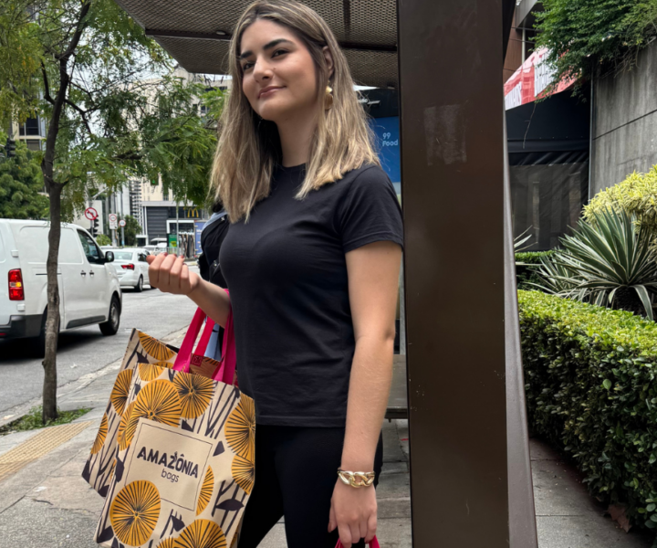 Mulher em área urbana segurando sacolas retornáveis estampadas após realizar compras.