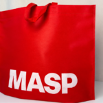 Sacola vermelha personalizada com a marca MASP em destaque, posicionada sobre uma superfície clara.