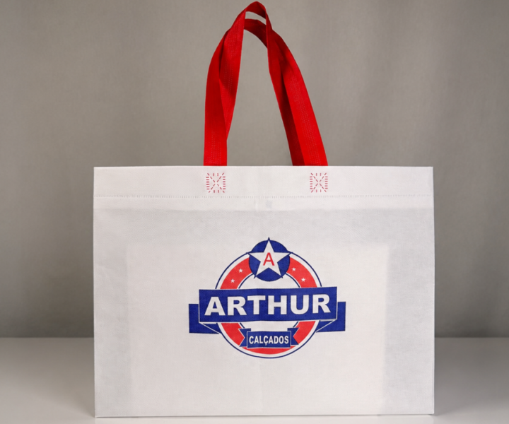 Sacola reutilizável branca com alças vermelhas e logotipo da Arthur Calçados estampado na parte frontal.